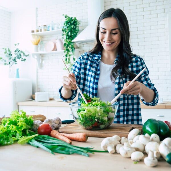 Beautiful young woman is preparing vegetable salad in the kitche